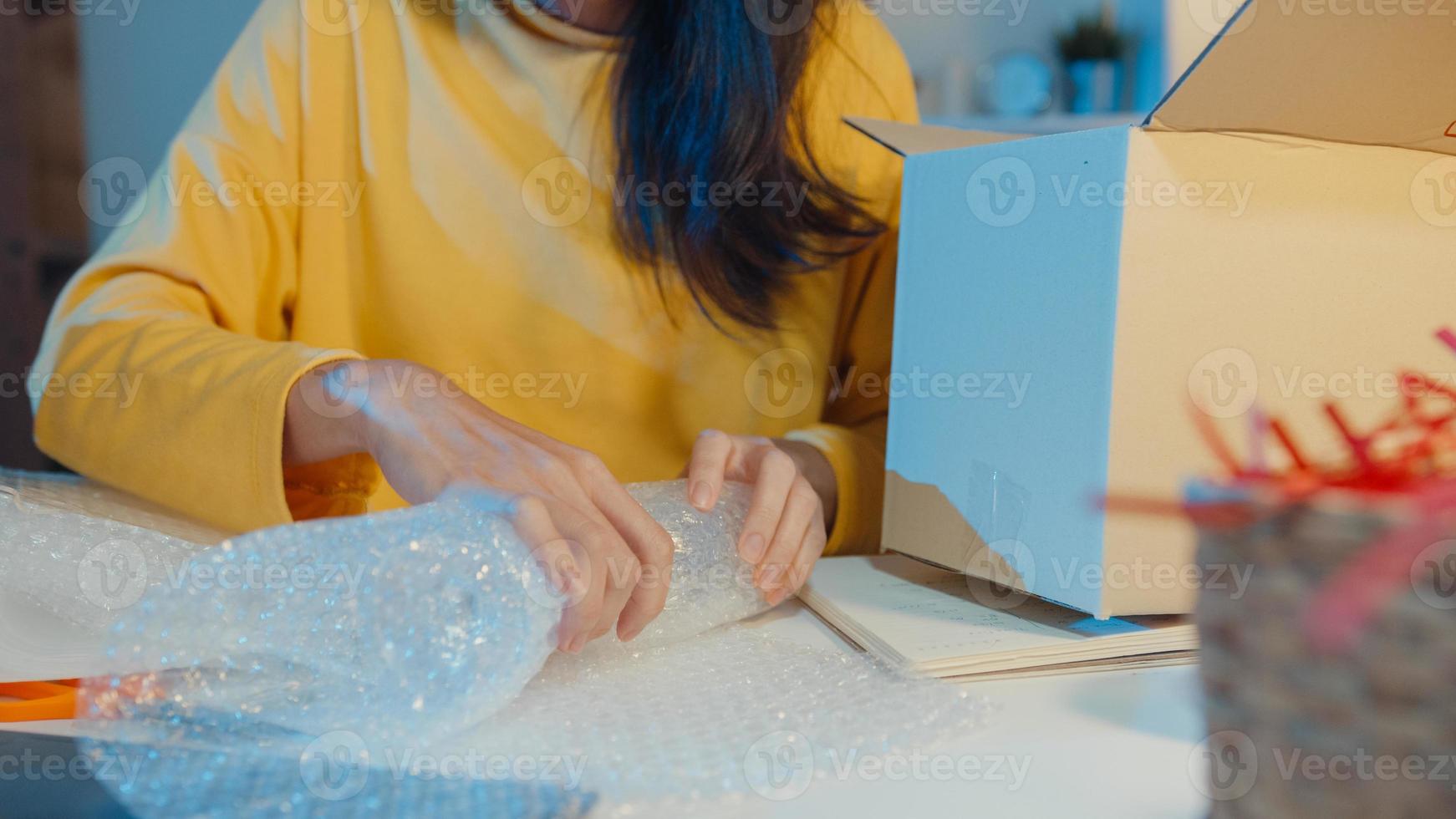 Young Asia businesswoman packing glass use bubble wrap for packing support damage fragile product in home office at night. Small business owner, online market delivery, lifestyle freelance concept. photo