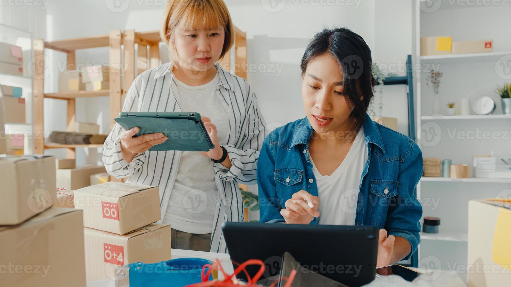 Young Asia businesswomen meeting check product purchase order on stock and save to tablet computer work at home office. Small business owner, online market delivery, lifestyle freelance concept. photo