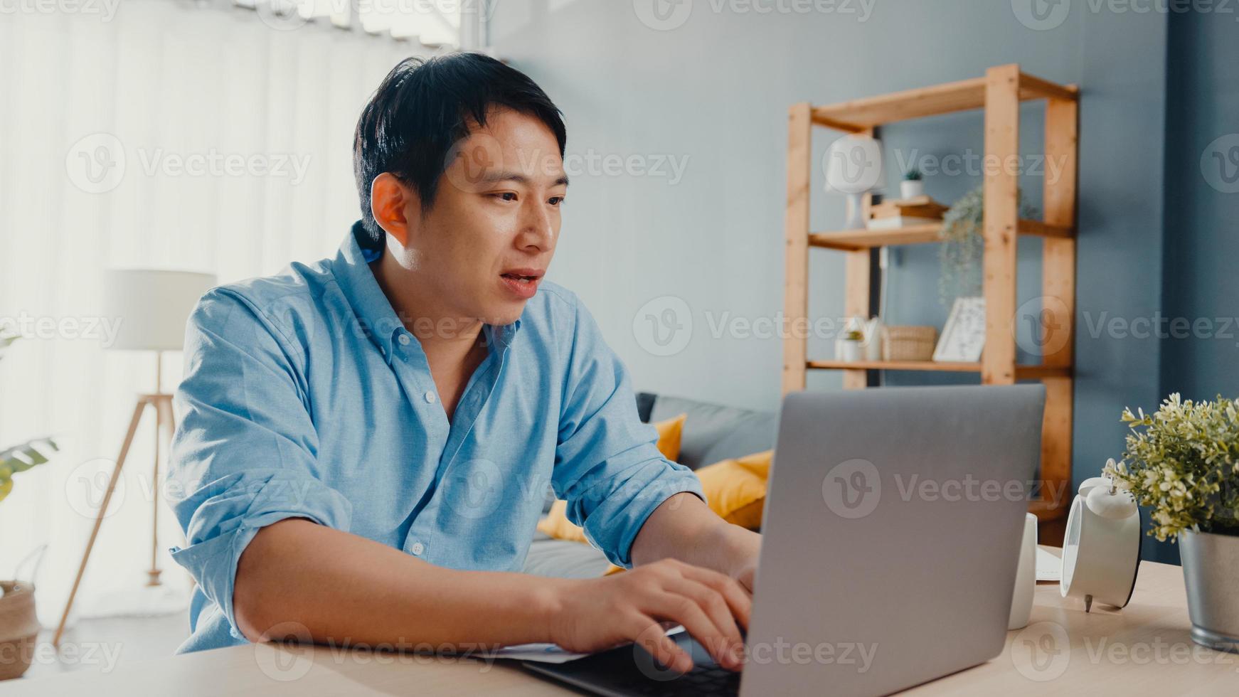 Freelance Asia guy casual wear using laptop online in living room at home office. Working from house, remotely work, distance education, social distancing, quarantine for corona virus prevention. photo