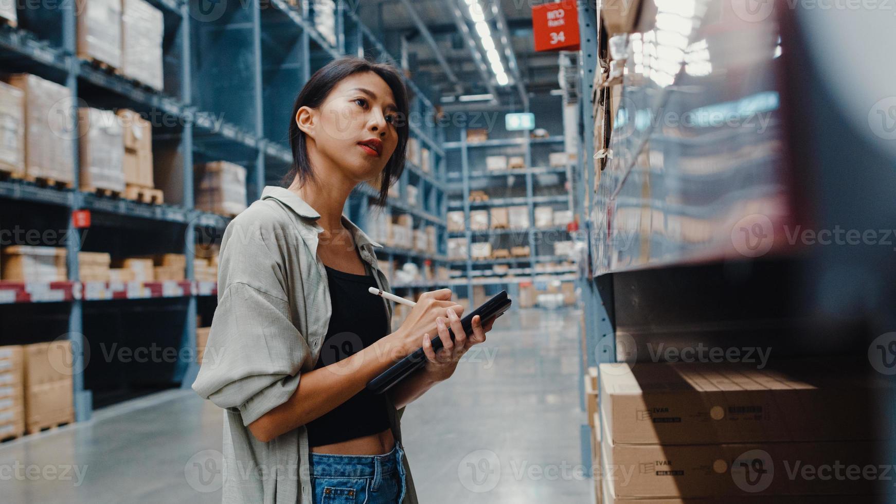 Attractive young Asia businesswoman manager looking for goods using digital tablet checking inventory levels standing in retail shopping center. Distribution, Logistics, Packages ready for shipment. photo