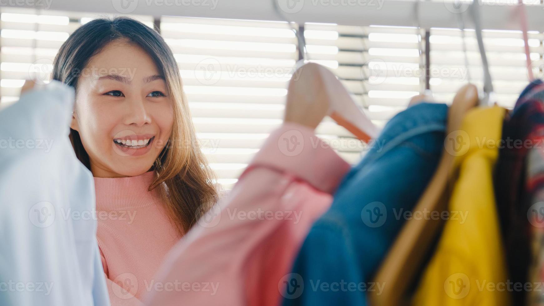 Beautiful attractive young Asia lady choosing her fashion outfit clothes in closet at house or store. Girl think what to wear casual shirt. Home wardrobe or clothing shop changing room. photo