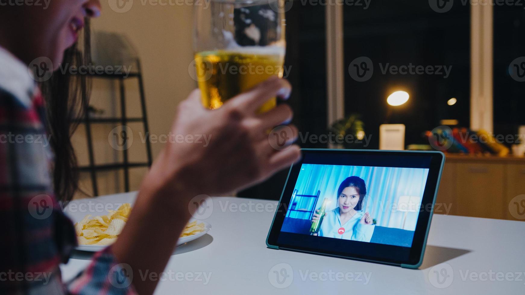 Young Asia lady drinking beer having fun happy moment night party event online celebration via video call in living room at home at night. Social distancing, quarantine for coronavirus prevention. photo