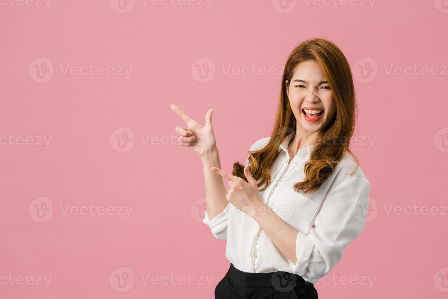 Retrato de joven asiática sonriendo con expresión alegre, muestra algo sorprendente en el espacio en blanco en ropa casual y mirando a cámara aislada sobre fondo rosa. concepto de expresión facial. foto