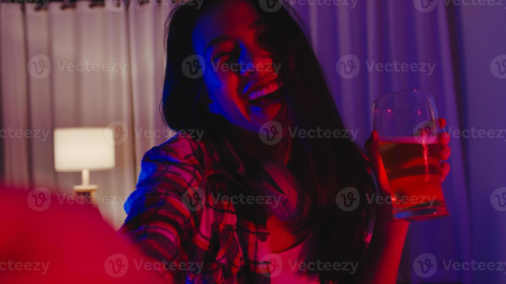 joven asiática bebiendo cerveza divirtiéndose momento feliz discoteca neón noche fiesta evento celebración en línea a través de videollamada en la sala de estar de casa. distanciamiento social, cuarentena para la prevención del coronavirus. foto