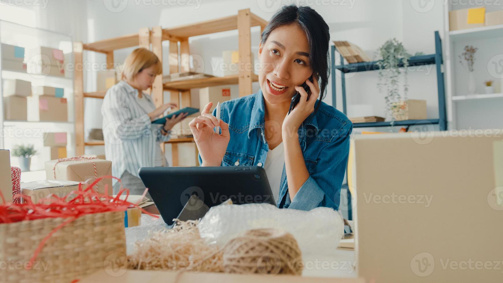 jóvenes empresarias asiáticas que usan llamadas de teléfono móvil para recibir órdenes de compra y verificar el producto en el trabajo de stock en la oficina en casa. propietario de una pequeña empresa, entrega de mercado en línea, concepto independiente de estilo de vida. foto