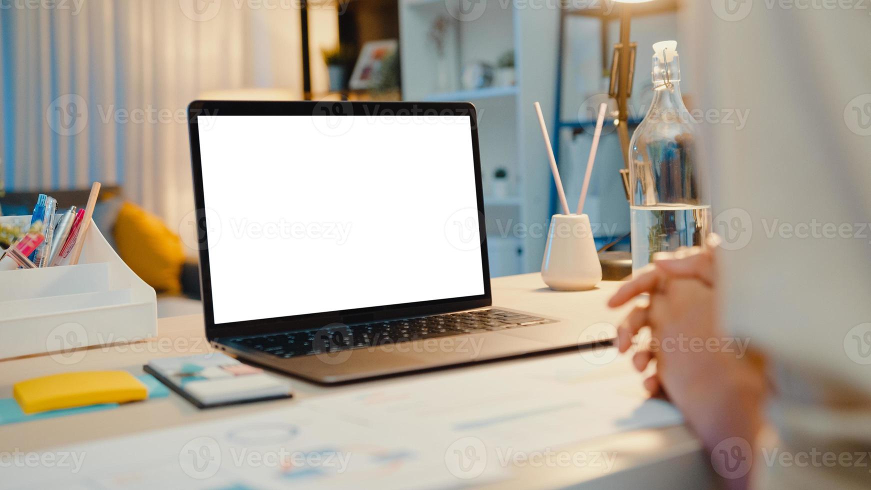 Asia businesswoman using laptop with blank white screen mock up display for advertising text talk to colleagues about plan in video call meeting at living room at house. Working overload at night. photo