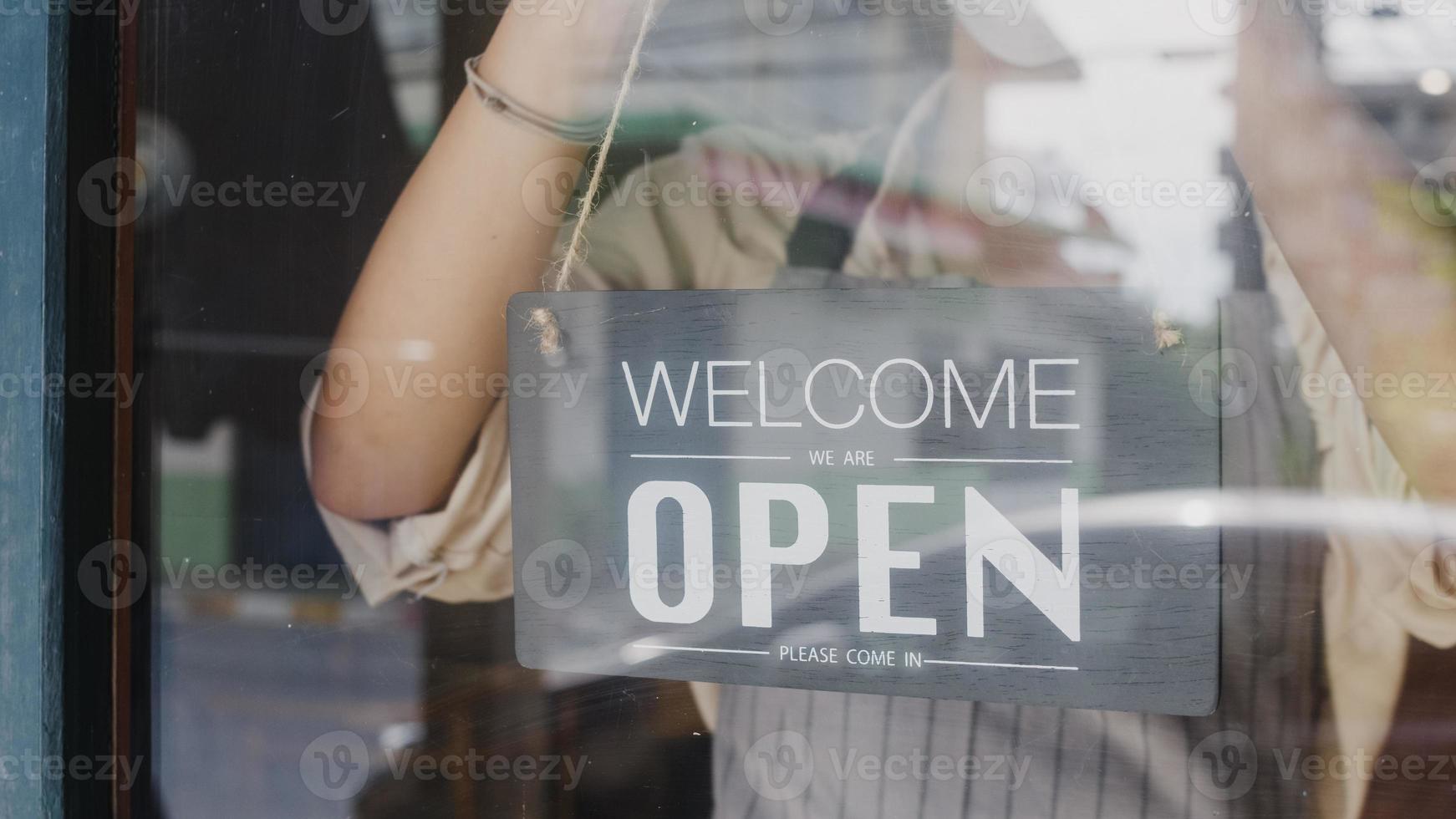 Young Asia girl wear face mask turning a sign from closed to open sign on door looking outside waiting for clients after lockdown. Owner small business, food and drink, business reopen again concept. photo