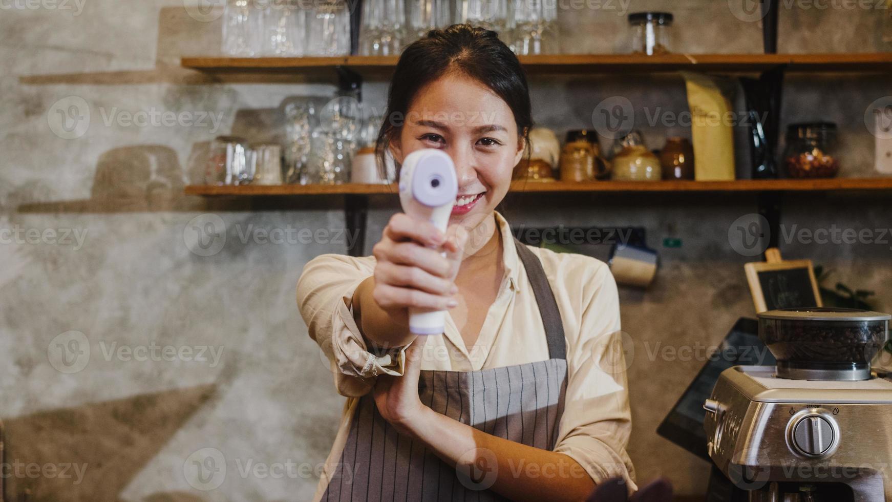 Portrait young Asia female restaurant staff using infrared thermometer checker or temperature gun on customer's forehead before enter at urban cafe restaurant. Lifestyle new normal after corona virus. photo