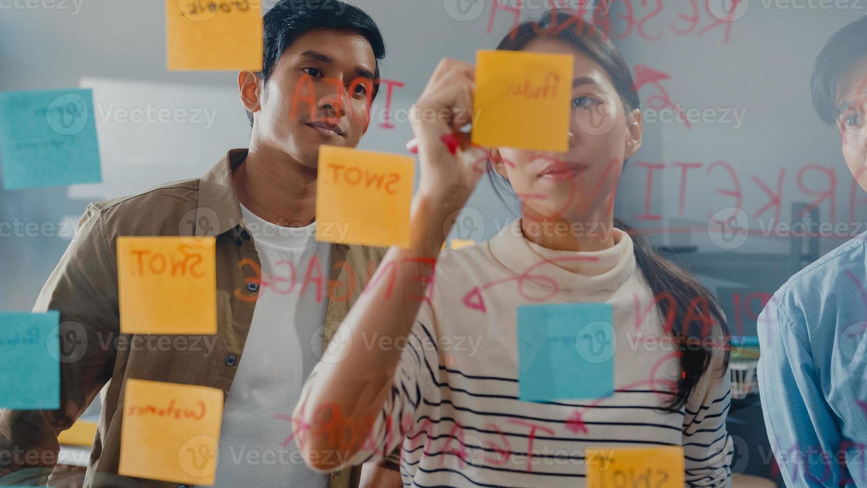 Asia businesspeople stand behind transparent glass wall listen manager pointing progress work and brainstorm meeting and worker post sticky note on wall at office. Business inspiration, Share ideas. photo