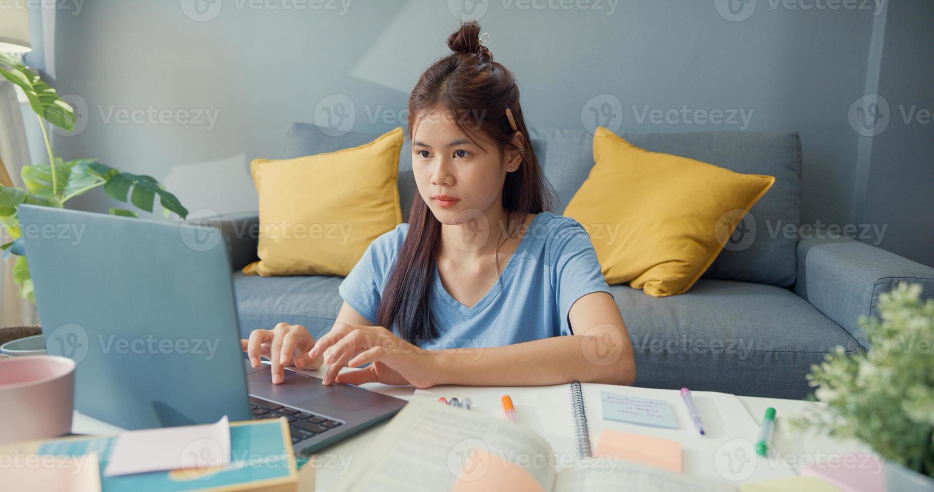 Young Asia girl teenager with casual use laptop computer learn online write lecture notebook for final test in living room at house. Isolate education online e-learning coronavirus pandemic concept. photo