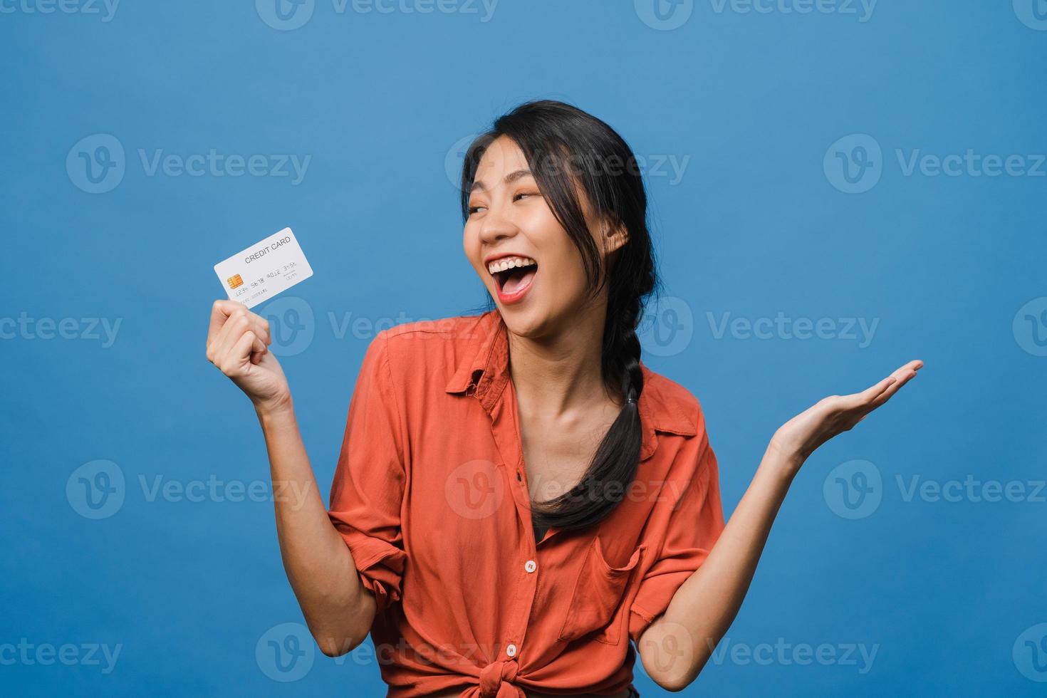 Young Asia lady show credit bank card with positive expression, smiles broadly, dressed in casual clothing feeling happiness and stand isolated on blue background. Facial expression concept. photo