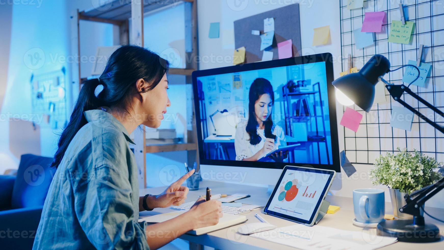 Asia businesswoman using desktop talk to colleagues about plan in video call meeting at living room. Working from house overload at night, remotely work, social distancing, quarantine for coronavirus. photo