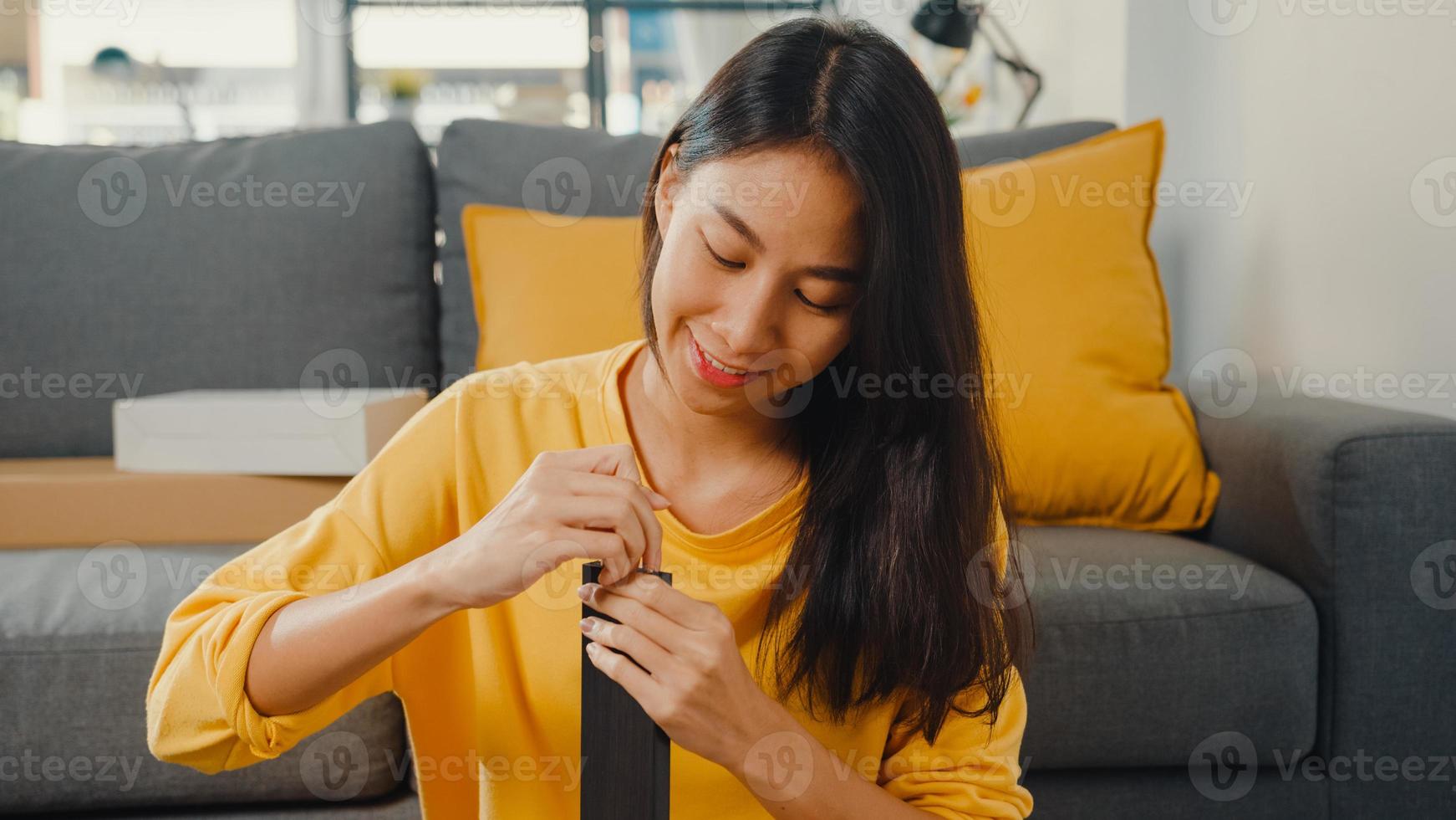 Feliz joven asiática desempacando la caja y leyendo las instrucciones para ensamblar muebles nuevos decorar la mesa de construcción de la casa con caja de cartón en la sala de estar de casa. foto