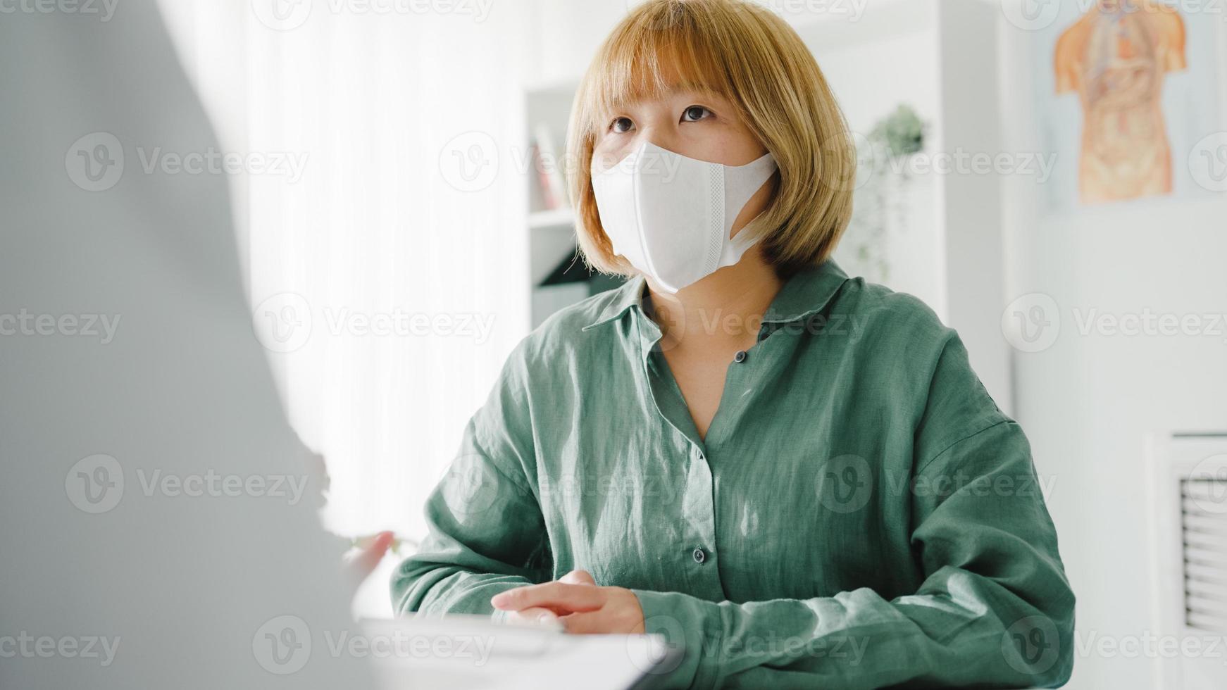 La joven doctora de Asia usa una máscara protectora usando el portapapeles está brindando una gran charla de noticias sobre los resultados o los síntomas con la paciente en la oficina del hospital. estilo de vida nuevo normal después del virus corona. foto