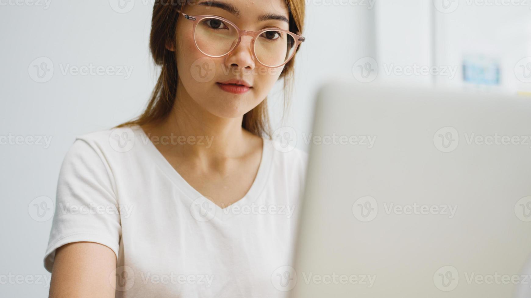 mujer de negocios asiática joven independiente ropa casual usando laptop trabajando en la sala de estar en casa. trabajo desde casa, trabajo a distancia, autoaislamiento, distanciamiento social, cuarentena para la prevención del coronavirus. foto
