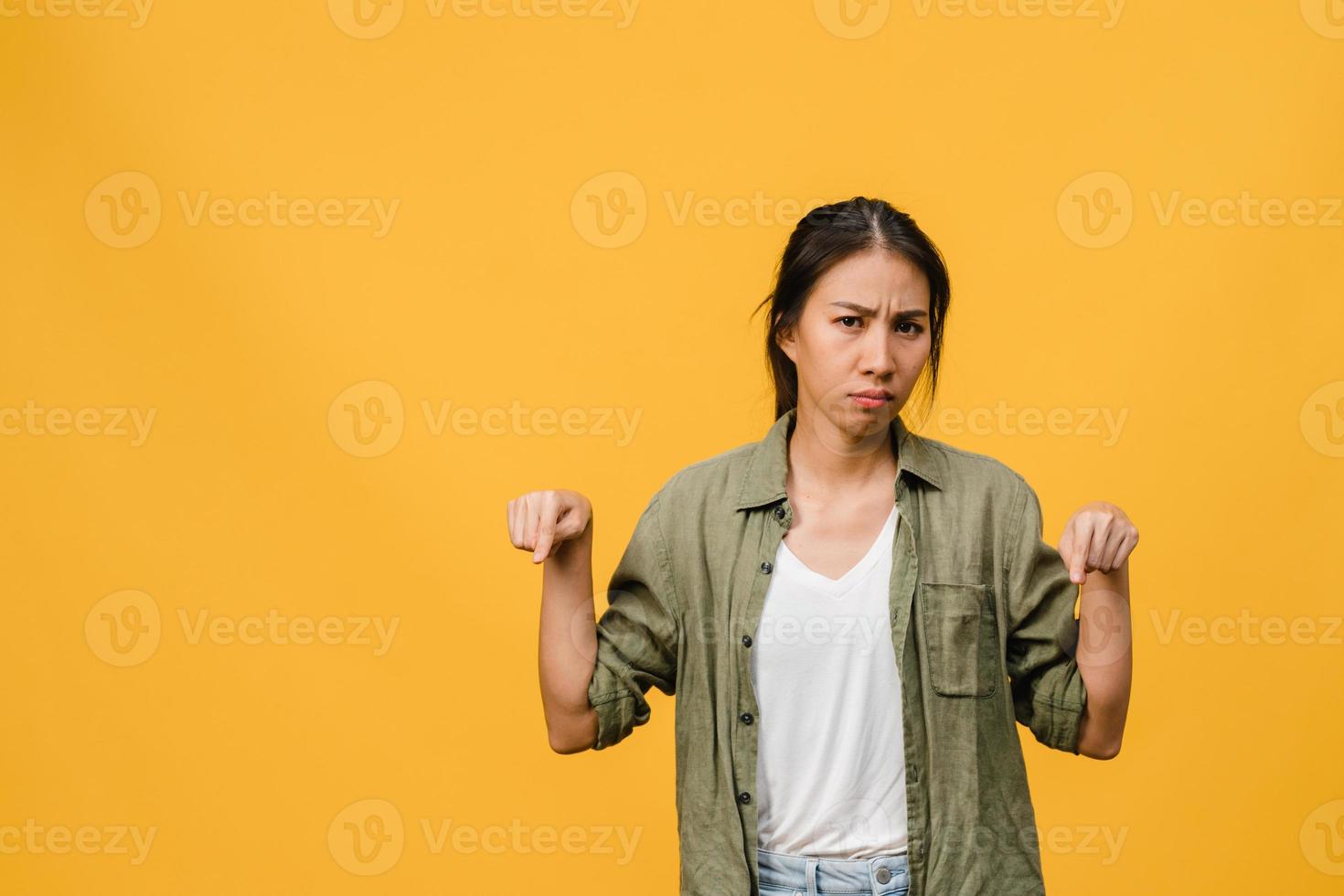 Young Asia Lady shows something amazing at blank space with negative expression, excited screaming, crying emotional angry looking at camera isolated over yellow background. Facial expression concept. photo