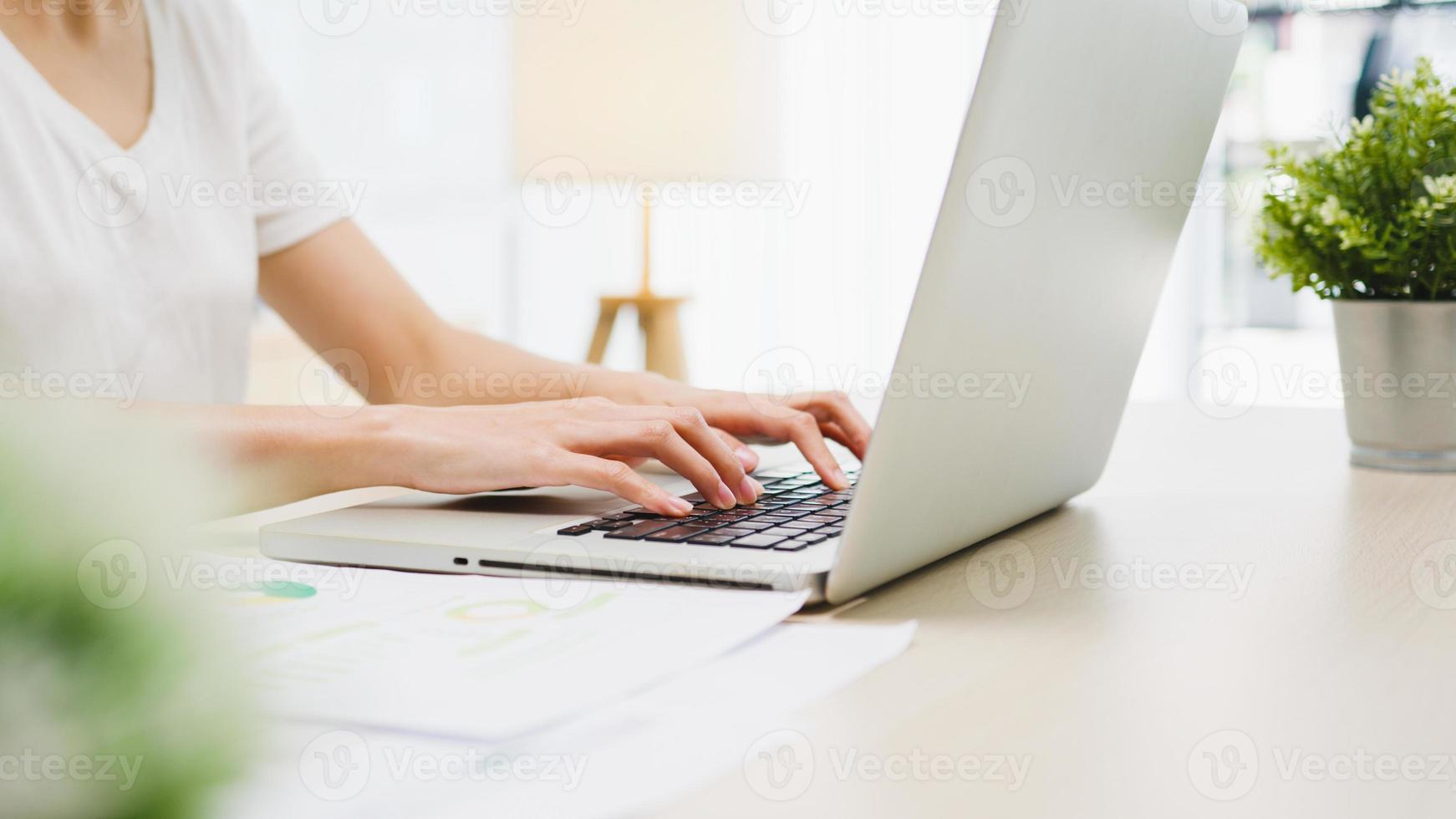 mujer de negocios asiática joven independiente ropa casual usando laptop trabajando en la sala de estar en casa. trabajo desde casa, trabajo a distancia, autoaislamiento, distanciamiento social, cuarentena para la prevención del coronavirus. foto