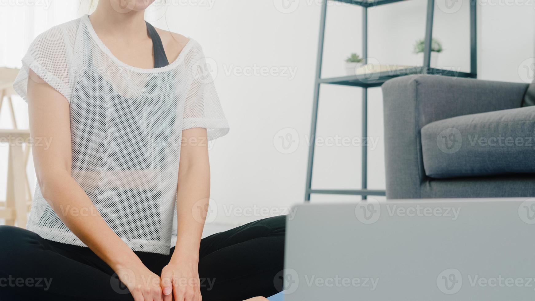 Young Korean lady in sportswear exercises doing working out and using laptop to watching yoga video tutorial at home. Distant training with personal trainer, social distance, online education concept. photo