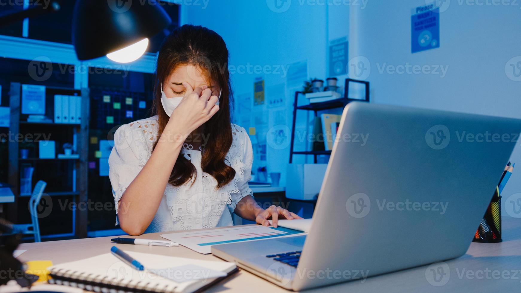 mujeres asiáticas independientes usan mascarilla usando una computadora portátil en el trabajo duro en la nueva oficina en casa normal. trabajando desde la sobrecarga de la casa por la noche, autoaislamiento, distanciamiento social, cuarentena para la prevención del virus corona. foto