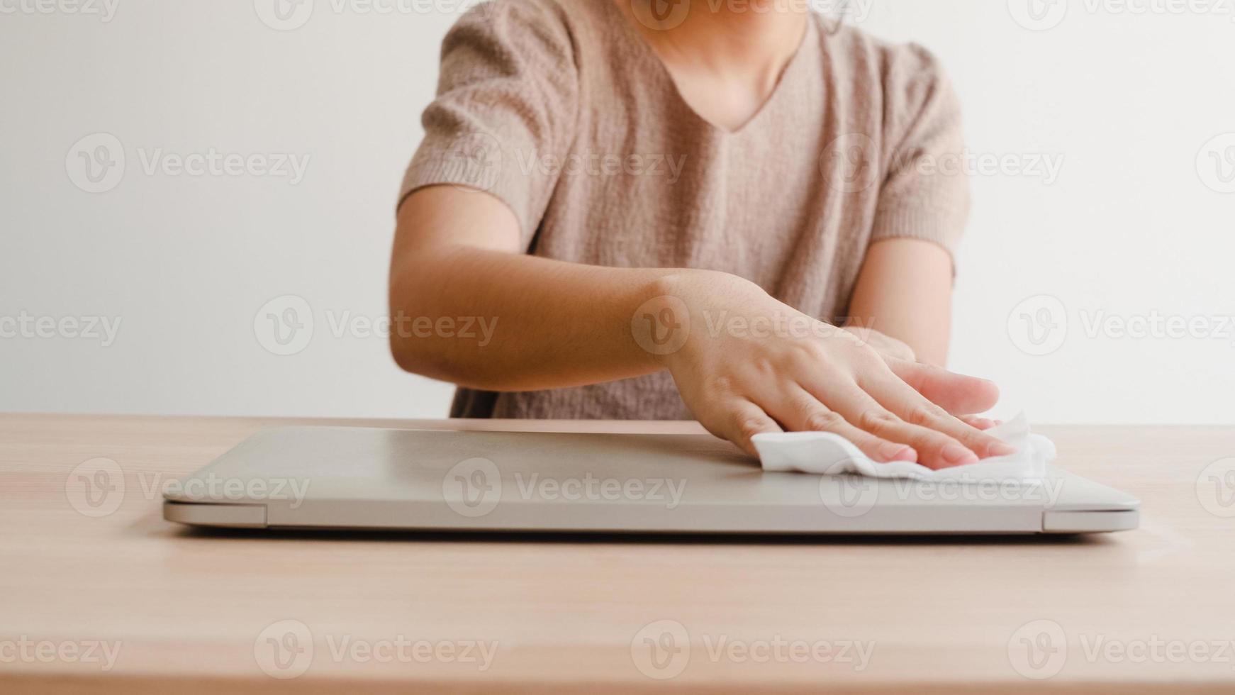 Asian woman using alcohol spray on tissue clean laptop before open for protect coronavirus. Female clean computer for hygiene when social distancing stay at home and self quarantine time. photo