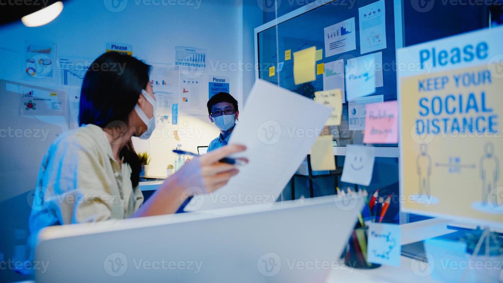 Feliz empresaria asiática usa mascarilla para el distanciamiento social en una nueva situación normal para la prevención de virus mientras se discute una reunión de lluvia de ideas de negocios juntos compartir datos en el trabajo en la noche de la oficina foto