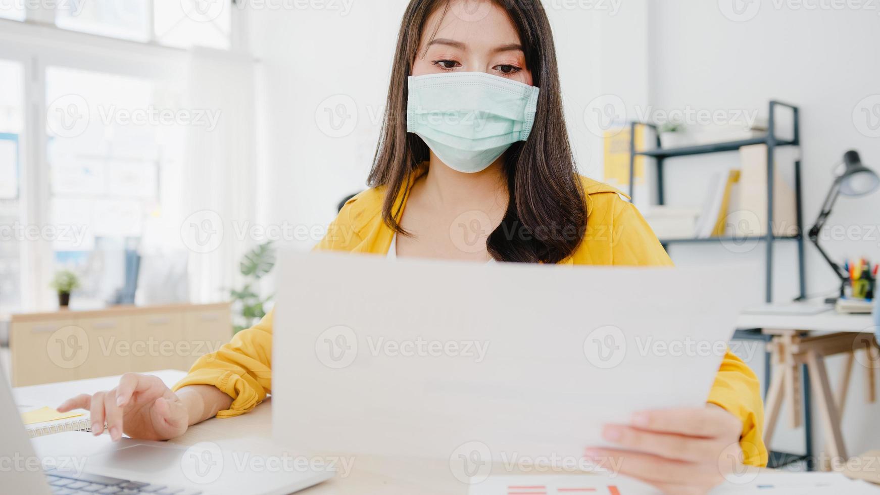 Asia empresaria emprendedora con mascarilla médica para el distanciamiento social en una nueva situación normal para la prevención de virus mientras usa la computadora portátil en el trabajo en la oficina. estilo de vida después del virus corona. foto