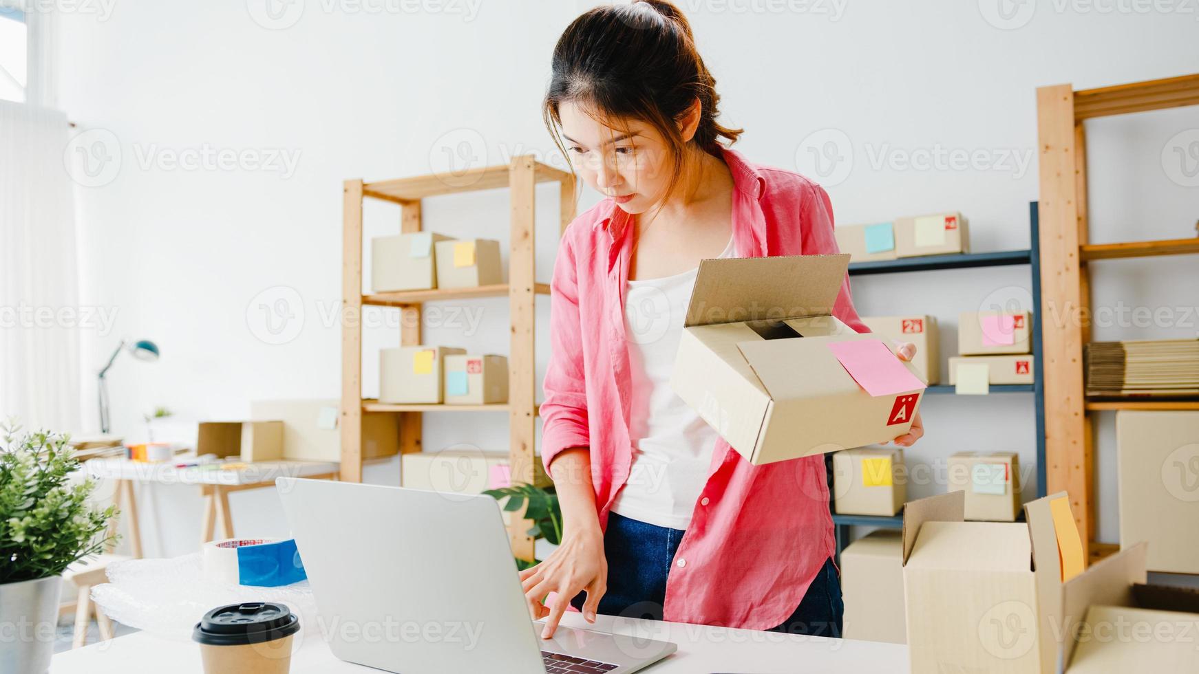 Young Asia entrepreneur businesswoman check product purchase order on stock and save to computer laptop work at home office. Small business owner, online market delivery, lifestyle freelance concept. photo