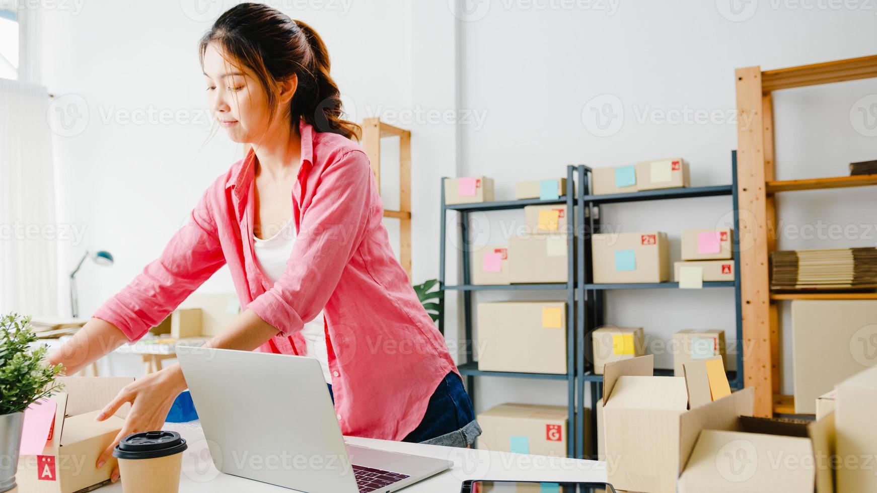 Young Asia entrepreneur businesswoman check product purchase order on stock and save to computer laptop work at home office. Small business owner, online market delivery, lifestyle freelance concept. photo