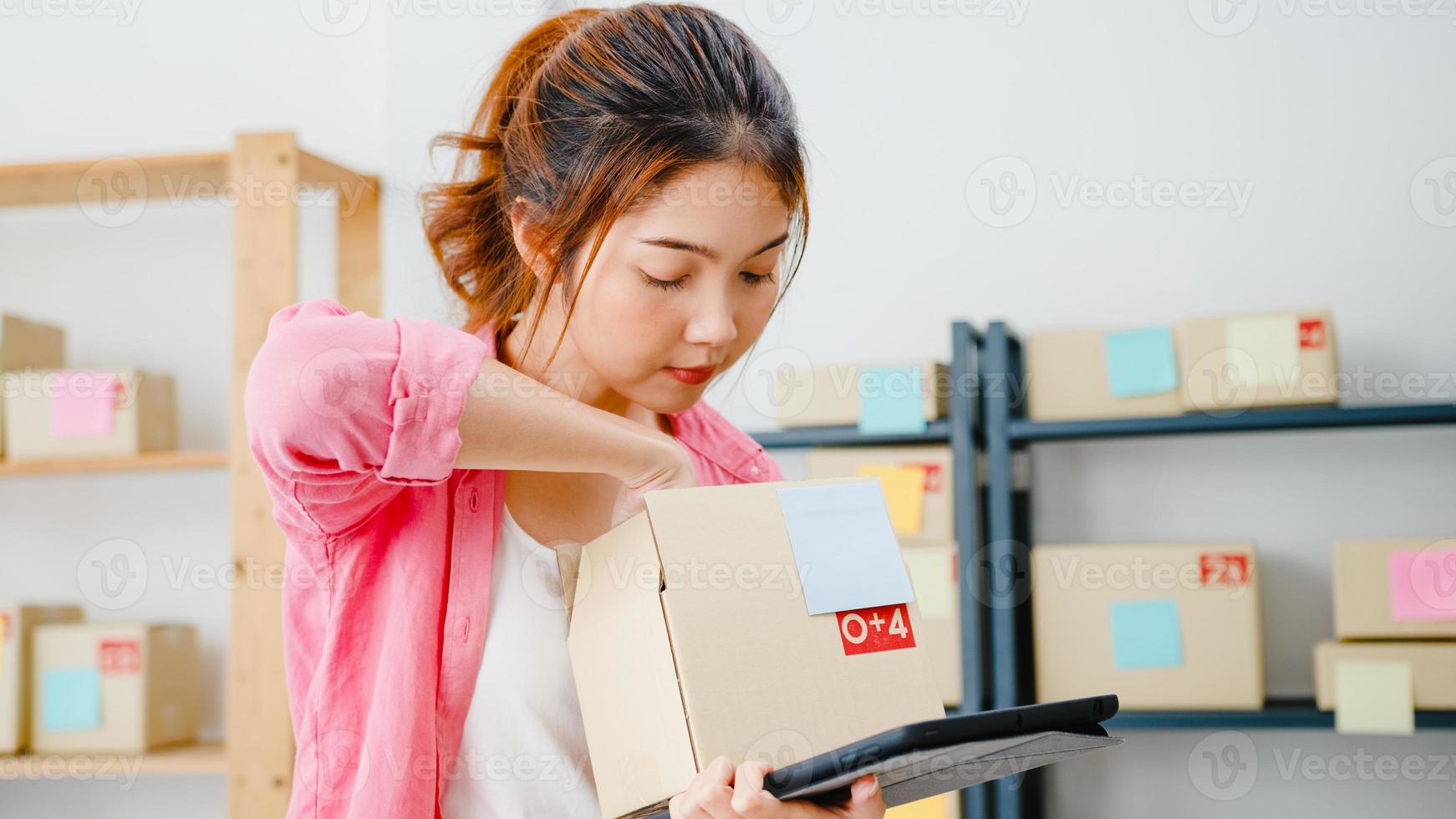 Young Asia entrepreneur businesswoman check product purchase order on stock and save to tablet computer work at home office. Small business owner, online market delivery, lifestyle freelance concept. photo