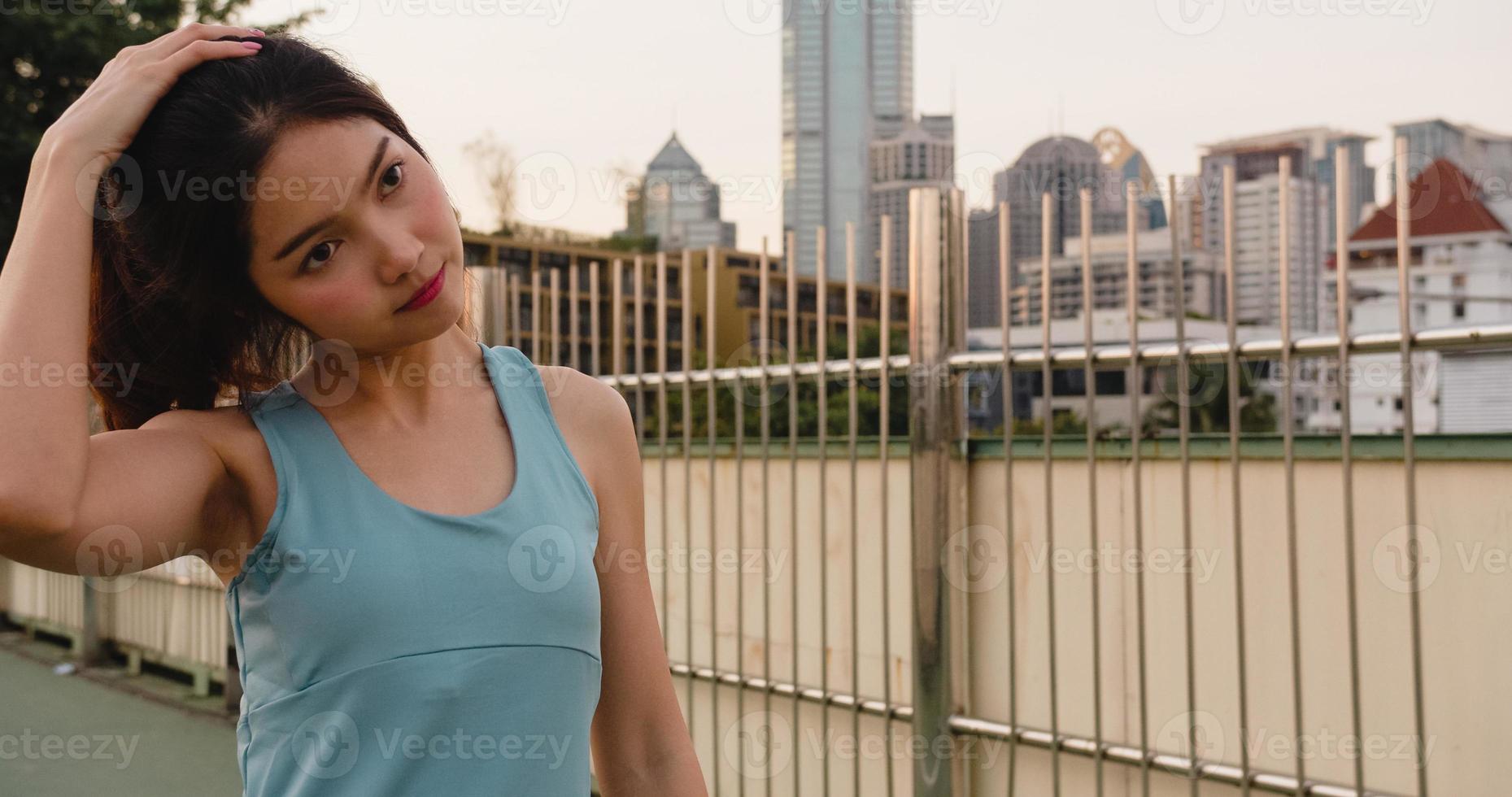 Beautiful young Asia athlete lady exercises doing stretch work out in urban environment. Japanese teen girl wearing sports clothes on walkway bridge in early morning. Lifestyle active sporty in city. photo