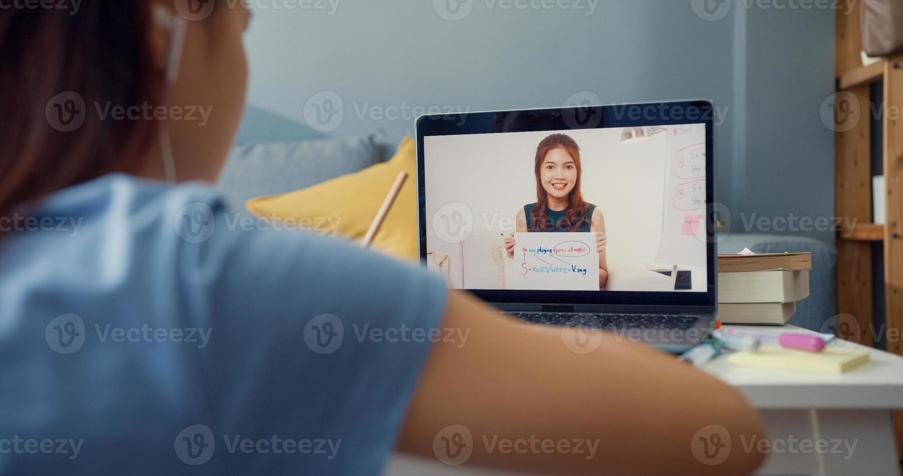Young Asia girl with casual use computer laptop video call learn online with teacher write lecture notebook living room at house. Isolate education online e-learning coronavirus pandemic concept. photo