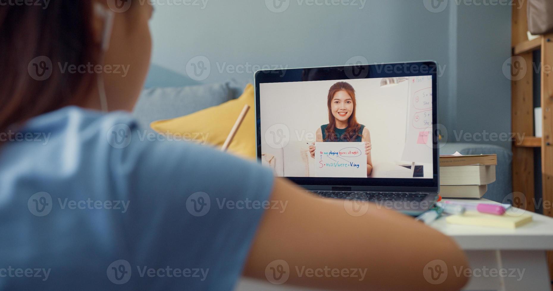 joven asiática con videollamada de computadora portátil de uso casual aprender en línea con el maestro escribir conferencia cuaderno sala de estar en casa. Aislar el concepto de pandemia de coronavirus de educación en línea e-learning. foto