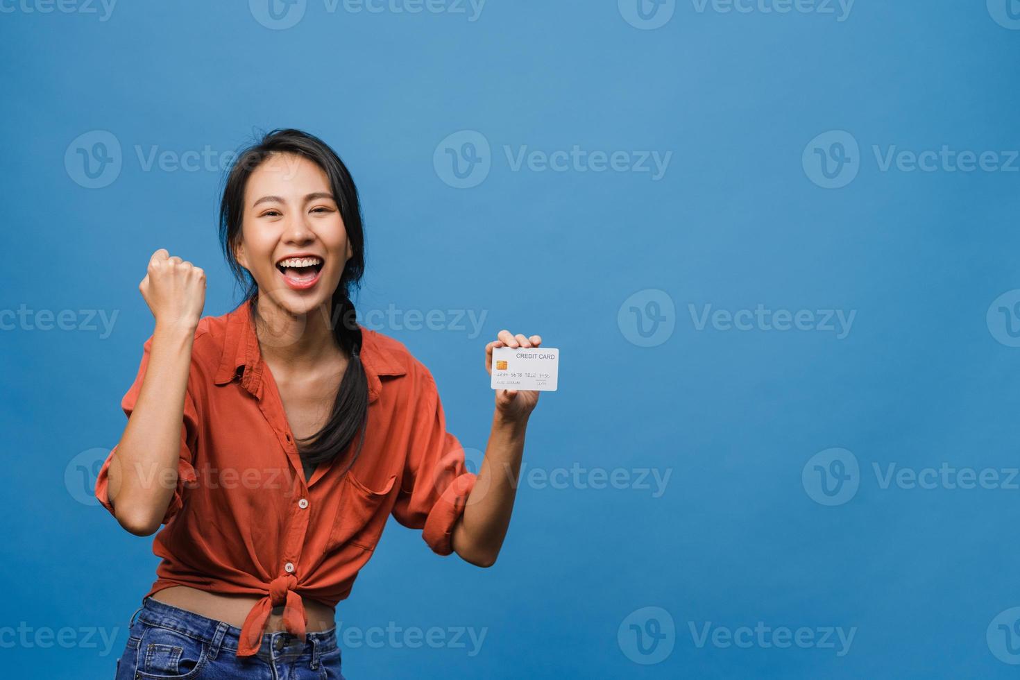 Young Asia lady show credit bank card with positive expression, smiles broadly, dressed in casual clothing feeling happiness and stand isolated on blue background. Facial expression concept. photo