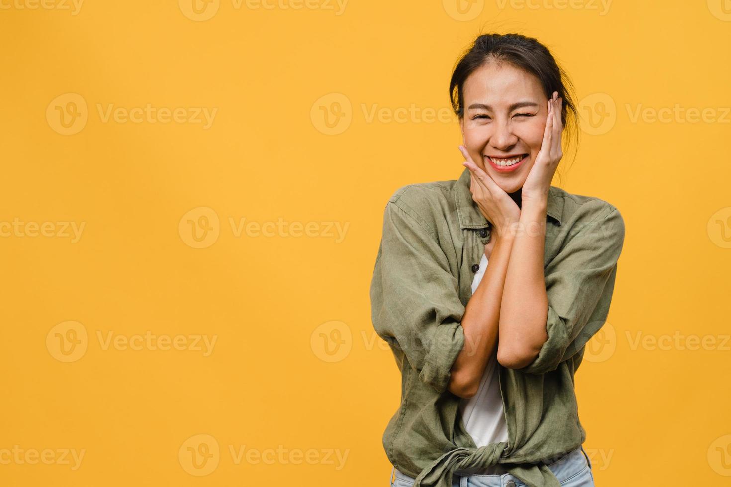 Jovencita asiática con expresión positiva, sonrisa amplia, vestida con ropa casual y mirando a cámara sobre fondo amarillo. feliz adorable mujer alegre se regocija con el éxito. concepto de expresión facial. foto