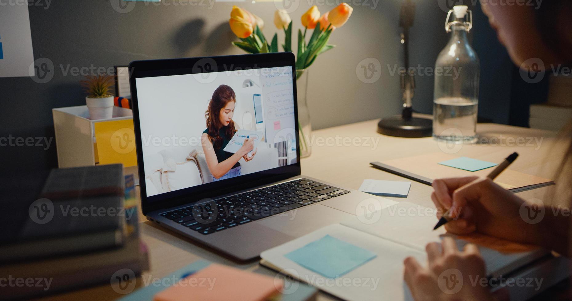 Young Asia teen girl student distance learning lesson with online teacher and study on laptop screen in living room at home night. Remotely, Social distancing, quarantine for corona virus prevention. photo