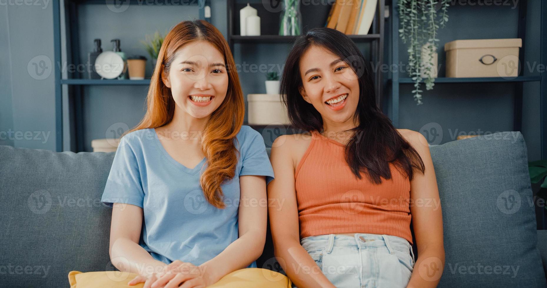 Teenager couple Asian women feeling happy smiling and looking to camera while relax in living room at home. Cheerful Roommate ladies video call with friend and family, Lifestyle woman at home concept. photo