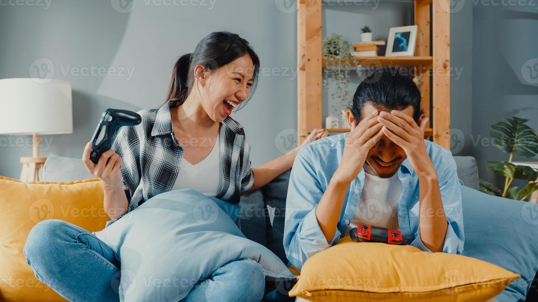 Feliz pareja de jóvenes de Asia, el hombre y la mujer se sientan en el sofá, usan el controlador de la palanca de mando, juegan un videojuego, pasan un tiempo divertido juntos en la sala de estar. estilo de vida familiar de pareja casada asiática, concepto de estancia de pareja en casa. foto