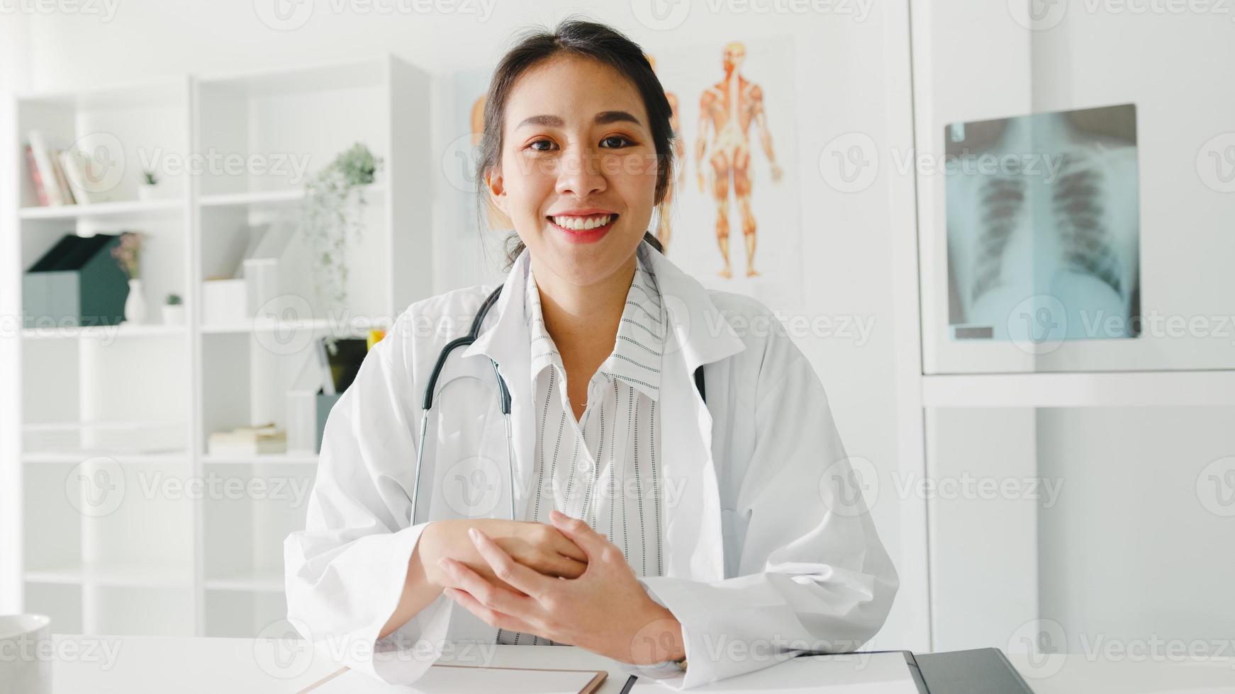 joven doctora de asia en uniforme médico blanco con estetoscopio usando computadora portátil hablar videoconferencia con el paciente, mirando a cámara en el hospital de salud. concepto de consulta y terapia. foto