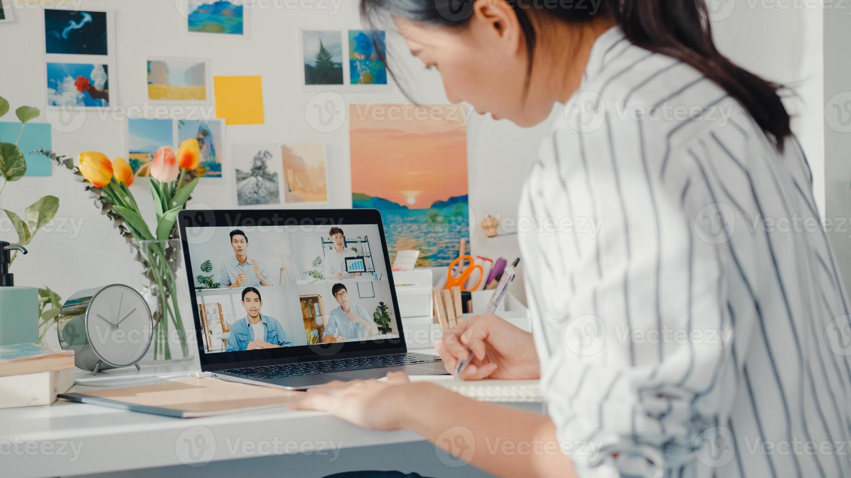 joven empleada de asia escucha al líder en la videollamada con diversos colegas multirraciales en línea con la computadora portátil en casa. la educación a distancia. alumna aprende en línea en casa, concepto de reunión en línea. foto