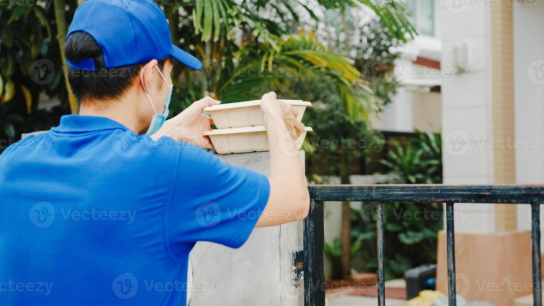 Young postal delivery courier man wear face mask handling food box for send to customer at house and Asian female receive delivered package outdoors. Lifestyle new normal after corona virus concept. photo