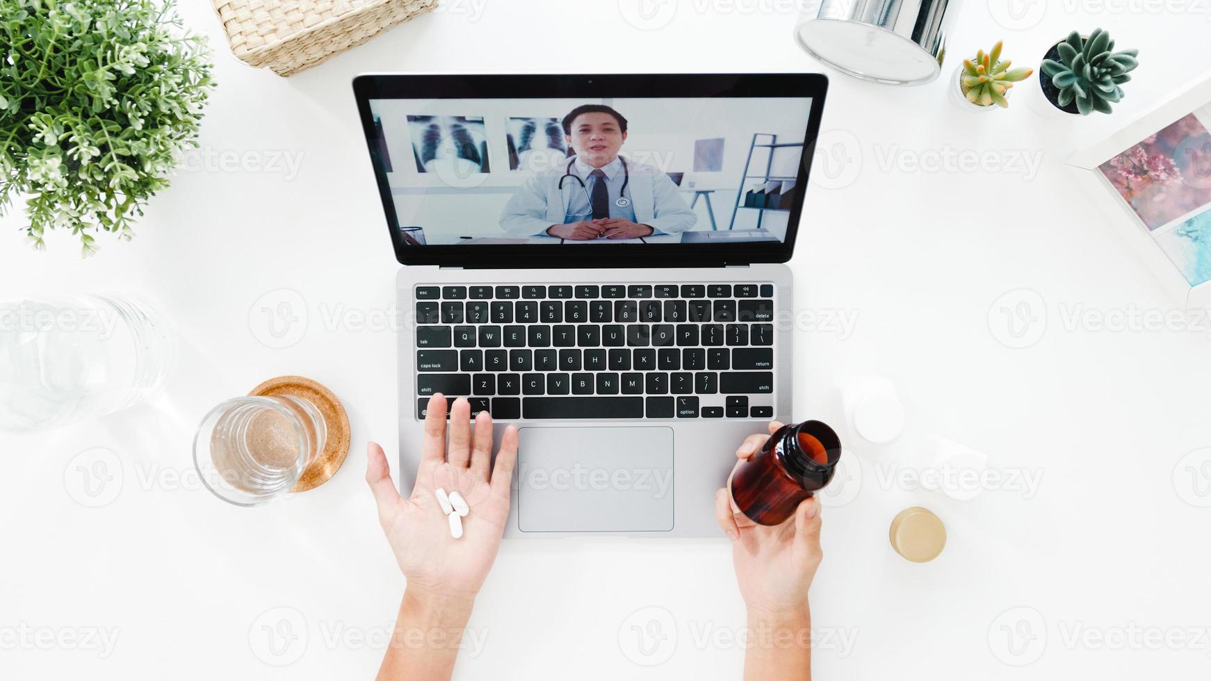Vista superior de una joven que usa una computadora portátil hablar sobre una enfermedad en una llamada de videoconferencia con una consulta en línea con un médico senior en la sala de estar de su casa. distanciamiento social, cuarentena por coronavirus. foto