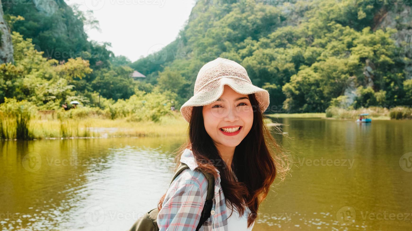 Cheerful young traveler Asian lady with backpack walking at the mountain lake. Korean teen girl enjoy her holidays adventure feeling happy freedom. Lifestyle travel and relax in free time concept. photo