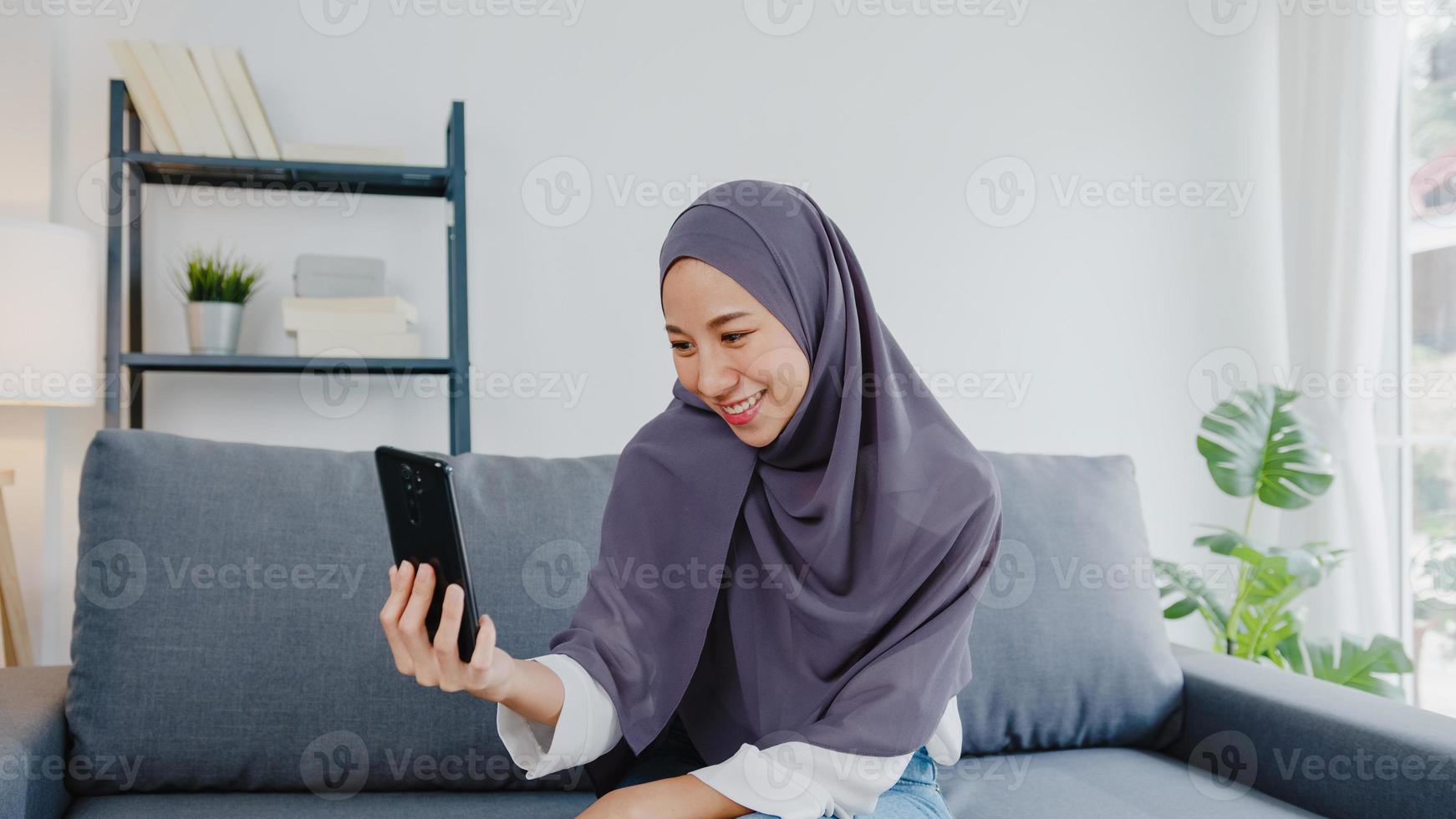 Asia muslim lady wear hijab using phone video call talking with couple at home. Young teenager making vlog video to social media on sofa in living room. Social distancing, quarantine for corona virus. photo