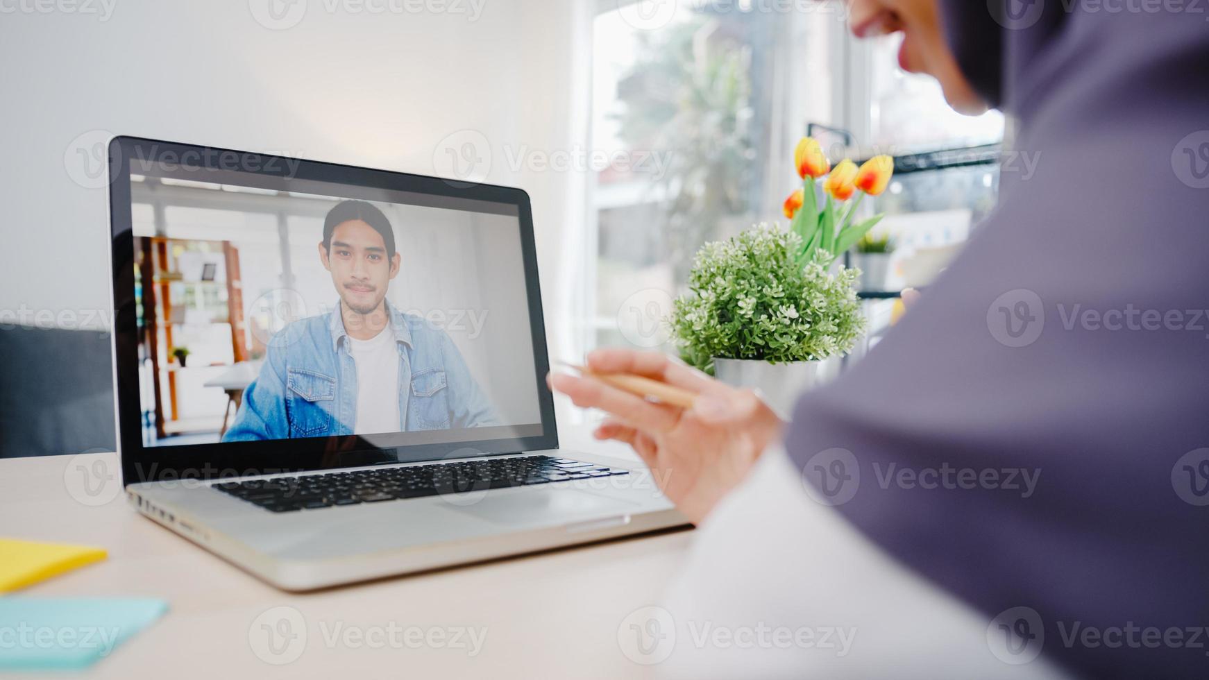 Asia muslim businesswoman using laptop talk to colleague about plan by video call brainstorm online meeting while remotely work from home at living room. Social distancing, quarantine for corona virus photo