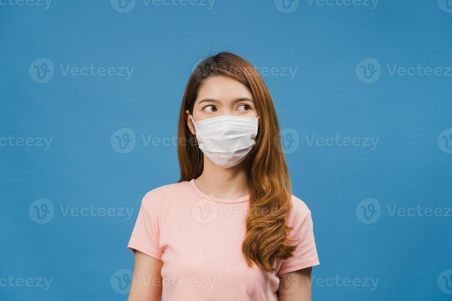 Young Asia girl wear medical face mask, tired of stress and tension, looks confidently at space isolated on blue background. Self-isolation, social distancing, quarantine for corona virus prevention. photo