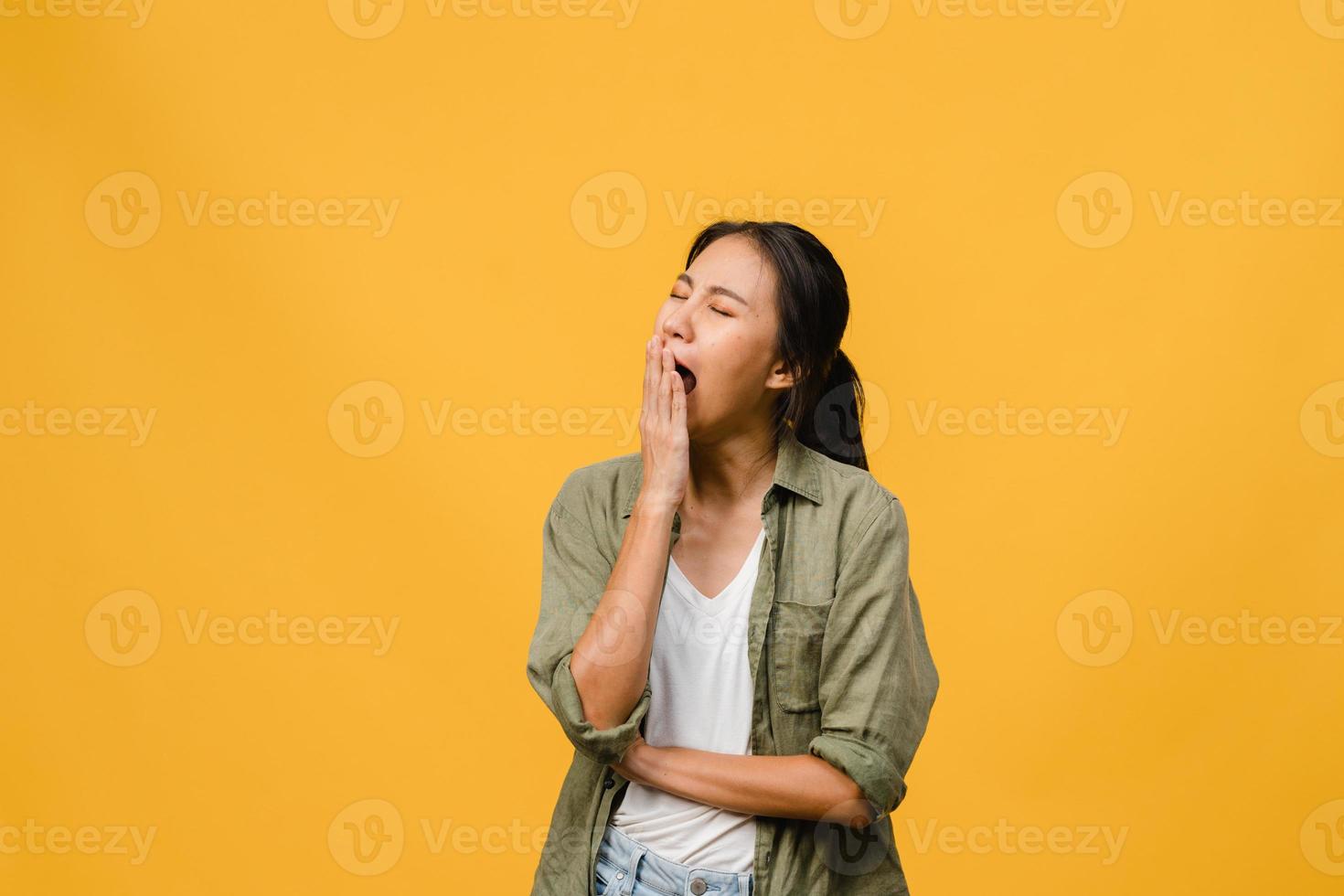 Portrait of Young Asia lady with negative expression, bored yawning tired covering mouth with hand in casual clothing isolated on yellow background with blank copy space. Facial expression concept photo