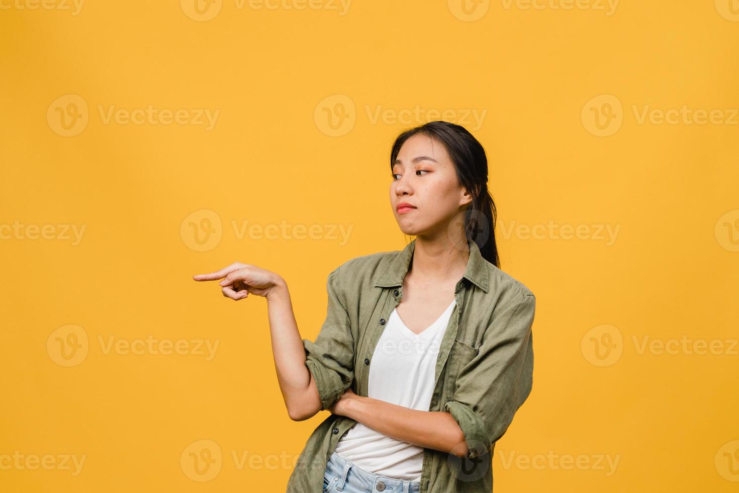 Joven mujer asiática muestra algo sorprendente en el espacio en blanco con expresión negativa, gritos emocionados, llorando enojado emocional en ropa casual aislada sobre fondo amarillo. concepto de expresión facial. foto