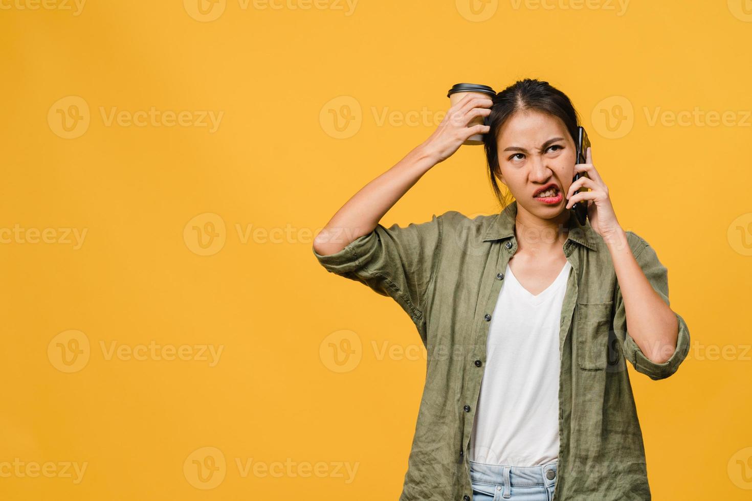 jovencita asiática habla por teléfono con expresión negativa, gritos emocionados, gritos emocionales enojados en ropa casual y se para aislado sobre fondo amarillo con espacio de copia en blanco. concepto de expresión facial. foto