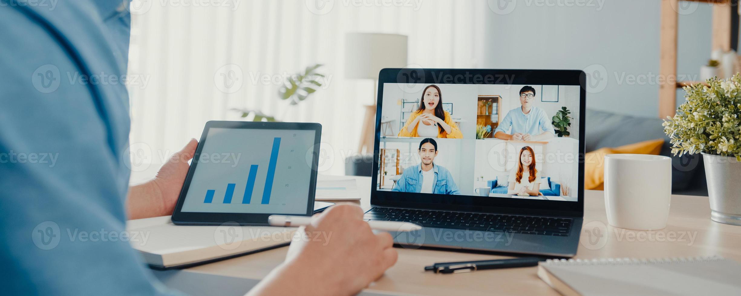 Young Asia businessman using laptop talk to colleagues about plan in video call meeting work from home at living room. Self-isolation, social distance, panoramic banner background with copy space. photo