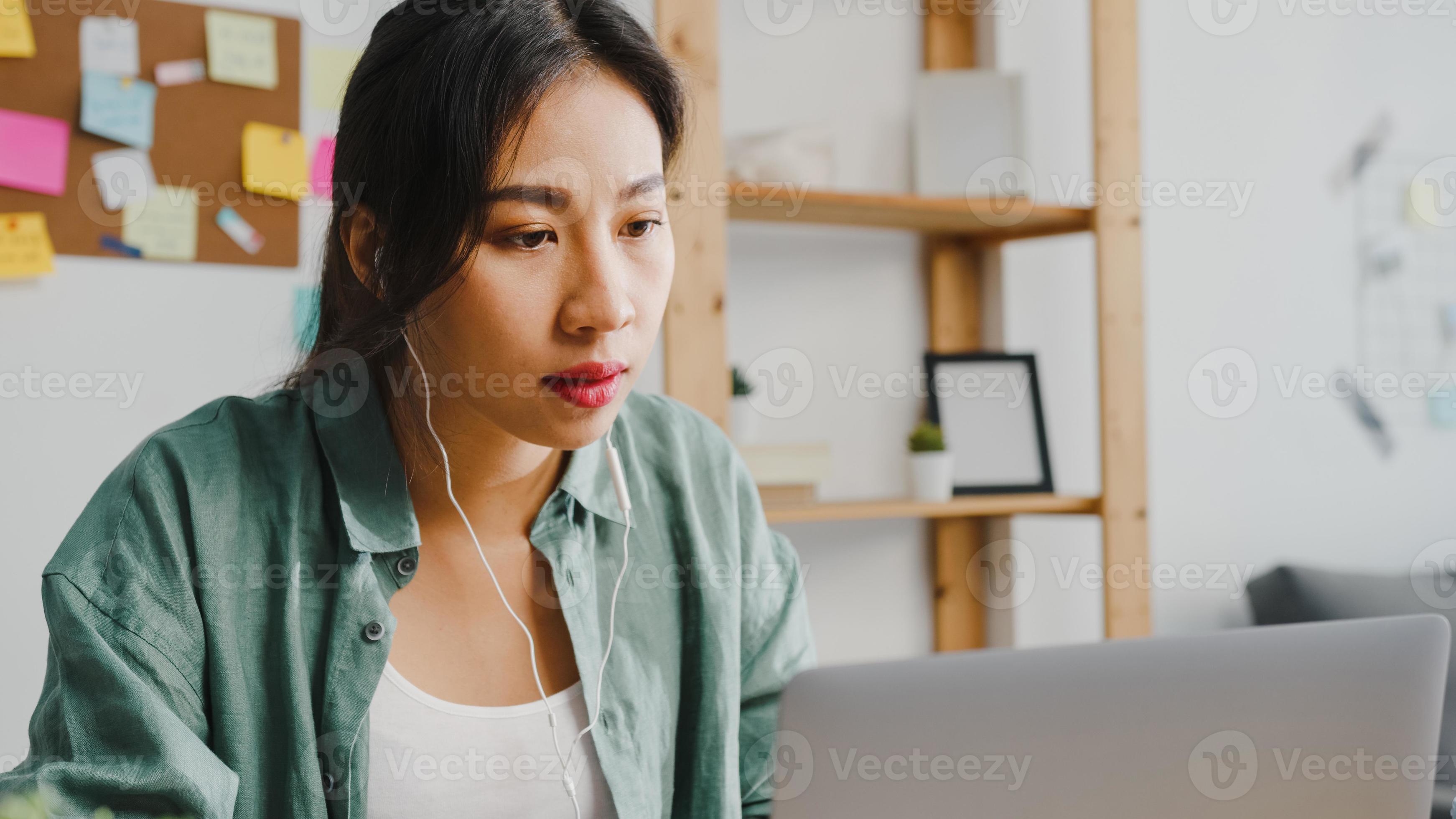Asia businesswoman using laptop talk to colleagues about plan in video call while smart working from home at living room. Self-isolation, social distancing, quarantine for corona virus prevention. photo